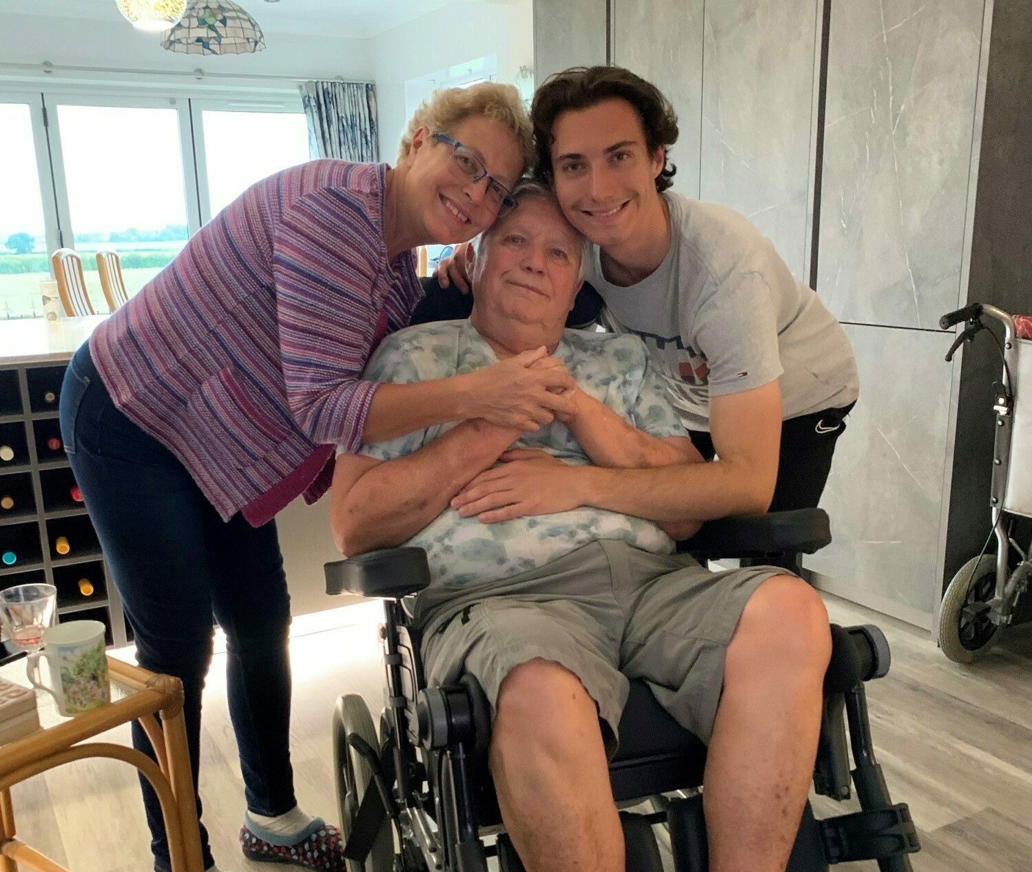 Pam and her son hugging her husband who is sat in a wheelchair