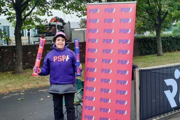 Volunteer Maria Rodriguez in front of a PSPA banner at the Great North Run