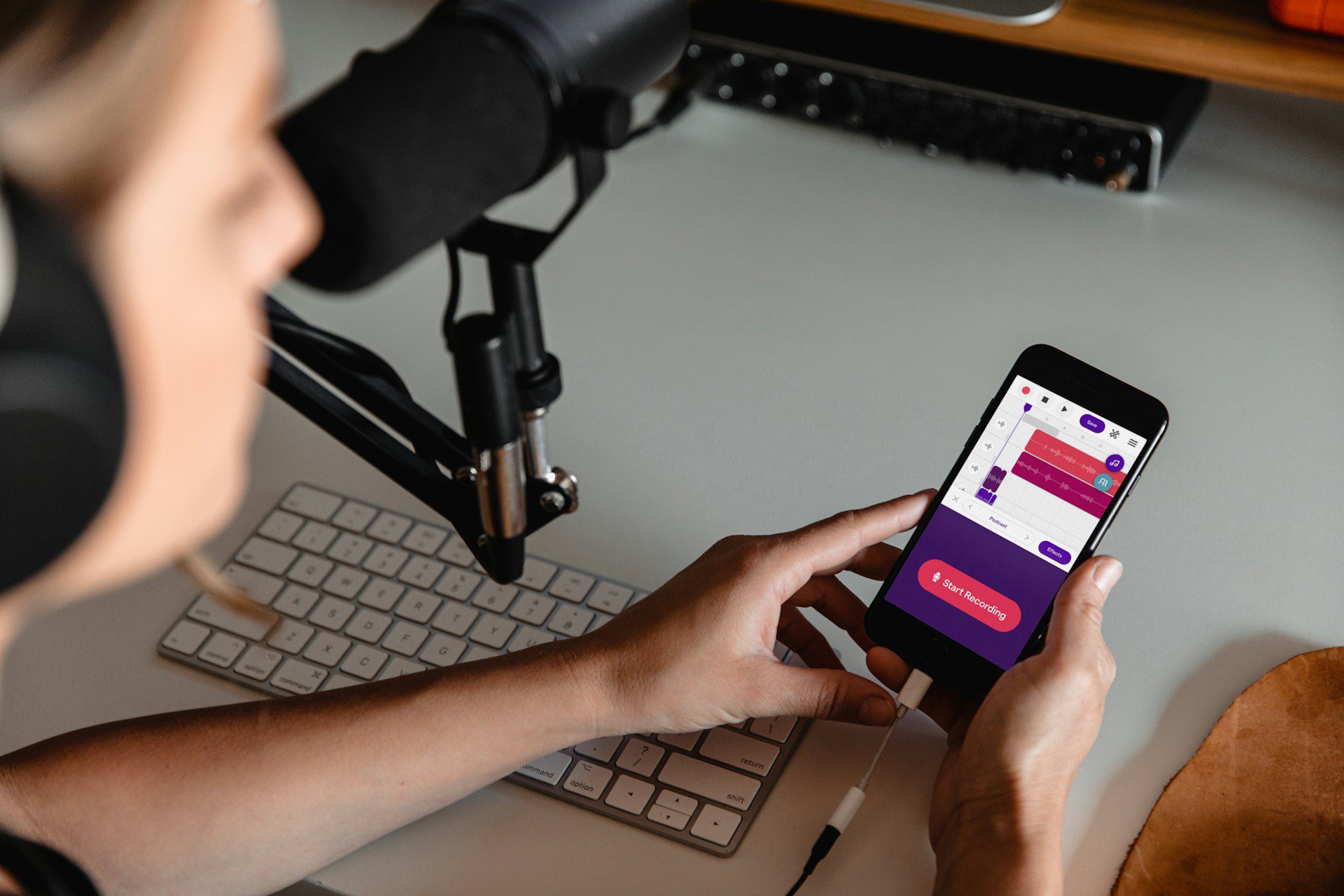 girl holding phone while recording with a mic and keyboard.